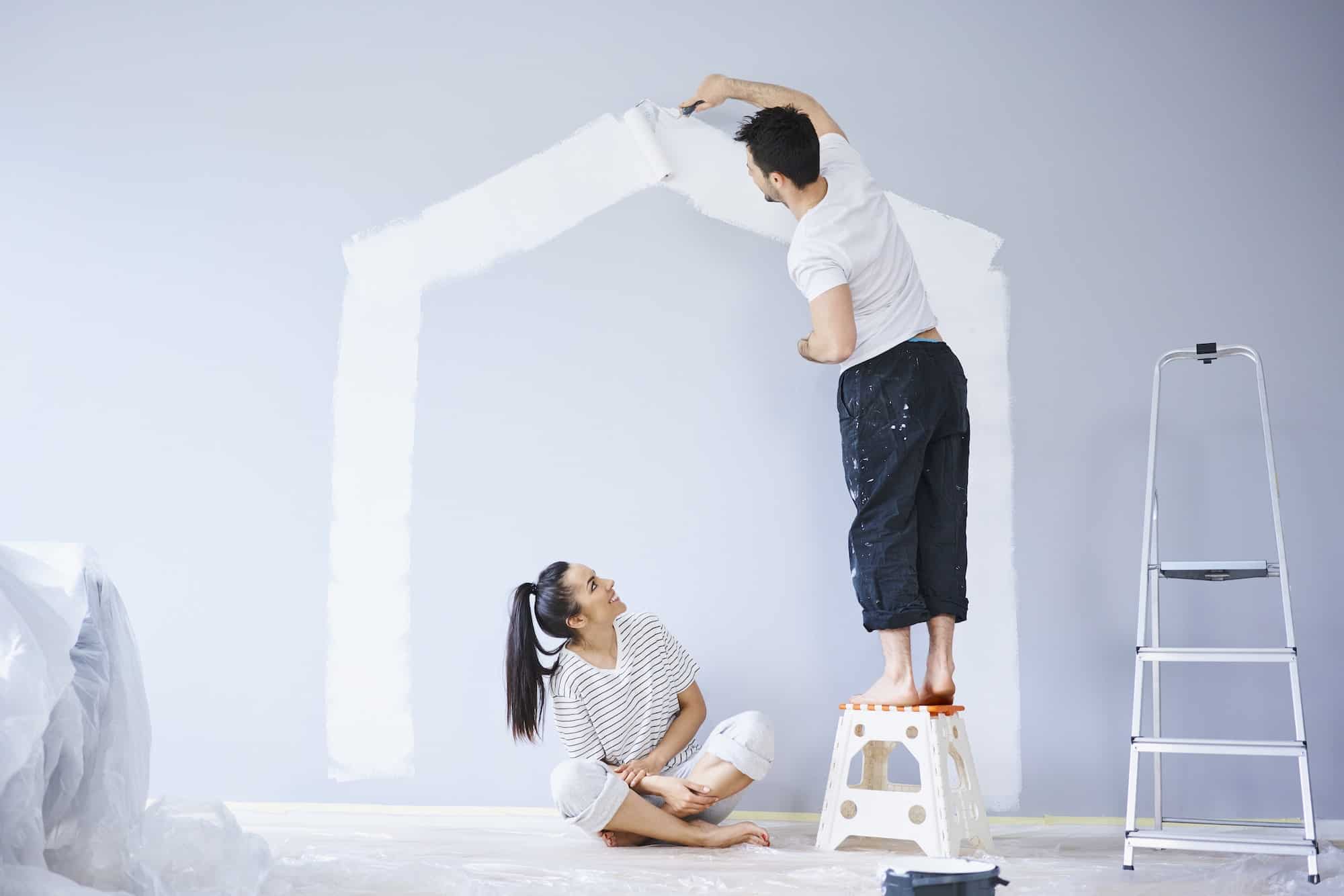 couple painting house shape on wall in new apartment